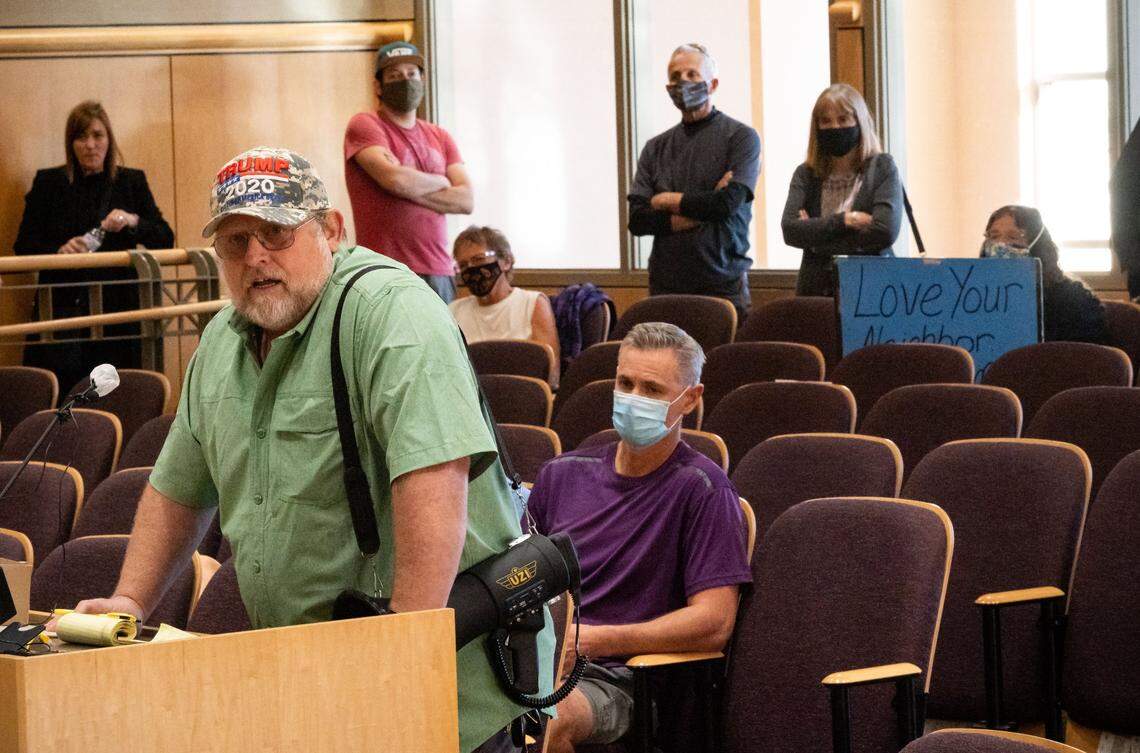 Mark Kent, of Shasta County, speaks against the state’s COVID-19 prevention measures during an extensive public comment session at the Shasta County Board of Supervisors meeting Thursday, Oct. 22, 2020, in Redding. “This is political and we all know it,” Kent said. “Are we going to start following illegal orders from a self-appointed king down in Sacramento?” Behind him, Marci Fernandes, right, of Shasta County, holds a sign saying “Love your neighbor” in support of coronavirus preventative measures. The board met to hear from the public before deciding how to react to county’s moving into the state’s most restrictive coronavirus risk tier.