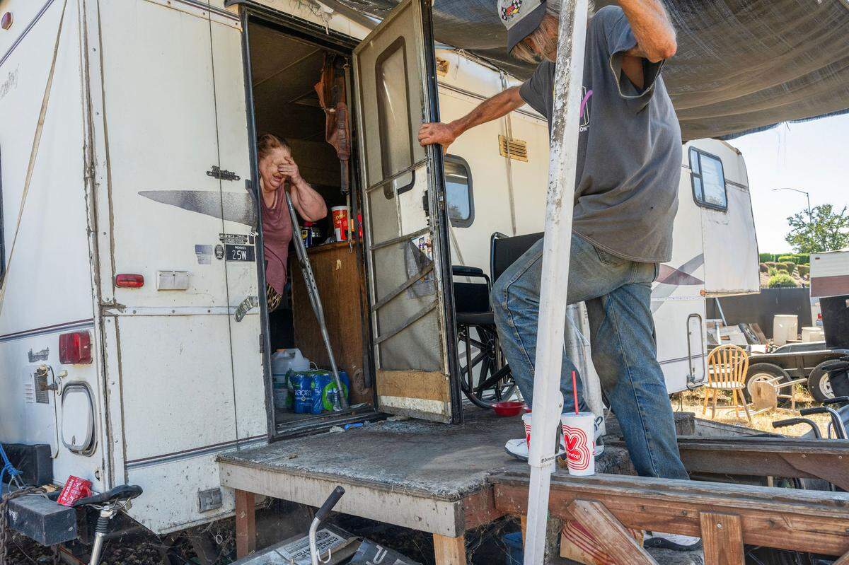 Camp Resolution resident Shonn Adams, 55, struggles to breathe as she exits her travel trailer with the help of resident Steven Goble earlier this month. Adams has chronic obstructive pulmonary disease and uses a portable oxygen machine. “We have generators out here running electricity for us, and I have to have it for my oxygen because I have to be on it all the time or I die,” said Adams.