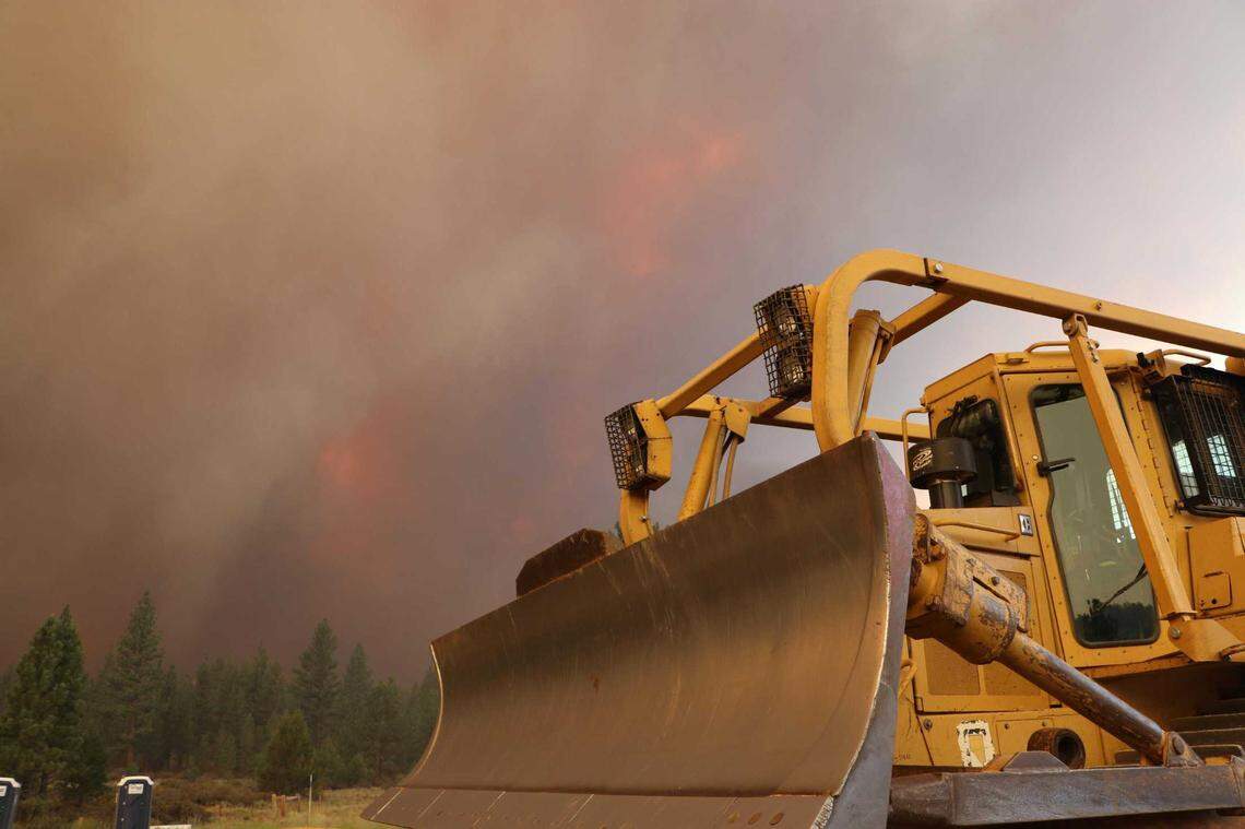 A bulldozer sits as a sentry as the Tamarack Fire burns across Highway 89 on Saturday, July 19, 2021. The wildfire has charred nearly 19,000 acres since bursting from a small blaze on Friday.
