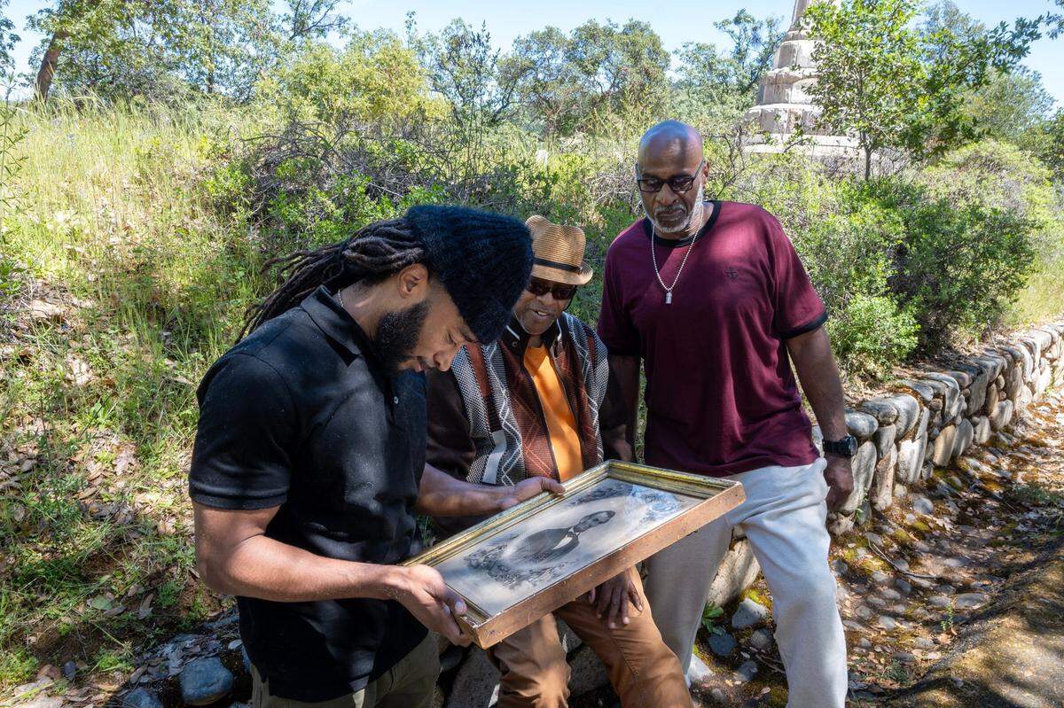 Dwayne Burgess Jr., left, Morgan Burgess and Dwayne Burgess Sr., right, view a photograph of Abraham Lincoln that was owned by their ancestor, Rufus Burgess, as they sit near the monument of James Marshall in Coloma in April. Rufus Burgess arrived to Coloma in 1850, where he mined gold in the river to buy his way out of bondage.