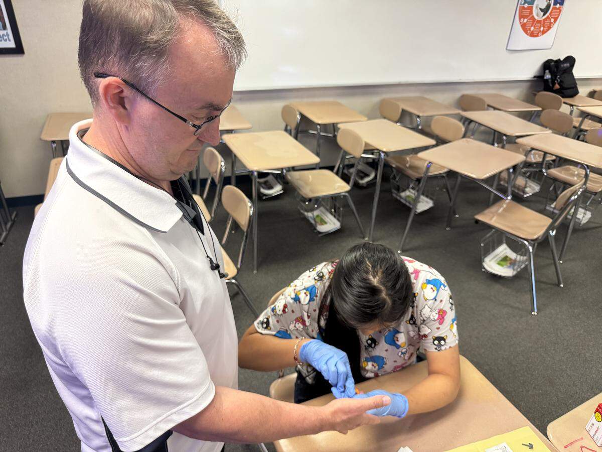 Valley High School teacher Rodney Black allows Health Tech Academy student Stephanie Castro to practice taking blood samples to use for a diagnostic test.