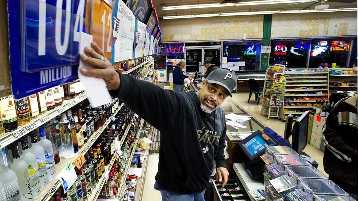 Clerk Walt Napier rubs a Mega Millions ticket on the $104 million sign for luck before giving it to his customer at Lichine’s Liquor and Deli in Sacramento in 2010. On Tuesday, March 20, 2024, lottery officials said a ticket worth $1.7 million was sold at the South Land Park retailer.