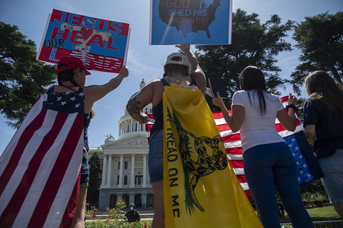 Protesters, wearing flags as capes, gather on 10th Street in Sacramento as the CHP prevents demonstrators from entering the Capitol grounds on Thursday, May 7, 2020, to rally against Gov. Gavin Newsom’s stay-at-home order during the coronavirus outbreak.