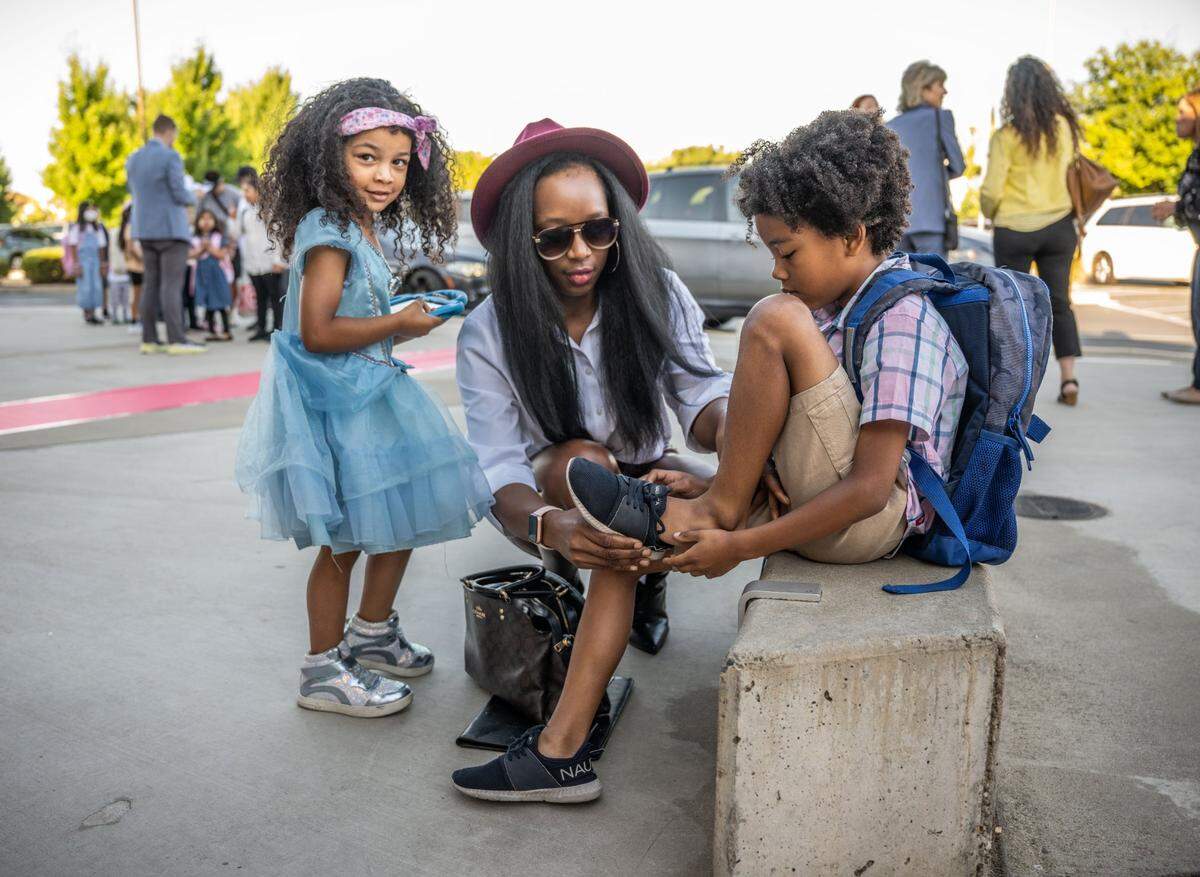 Shana Merceron, center, helps her son Elisha put on his shoes as sister Norah waits on the first day back to school at Navigator Elementary on Tuesday.