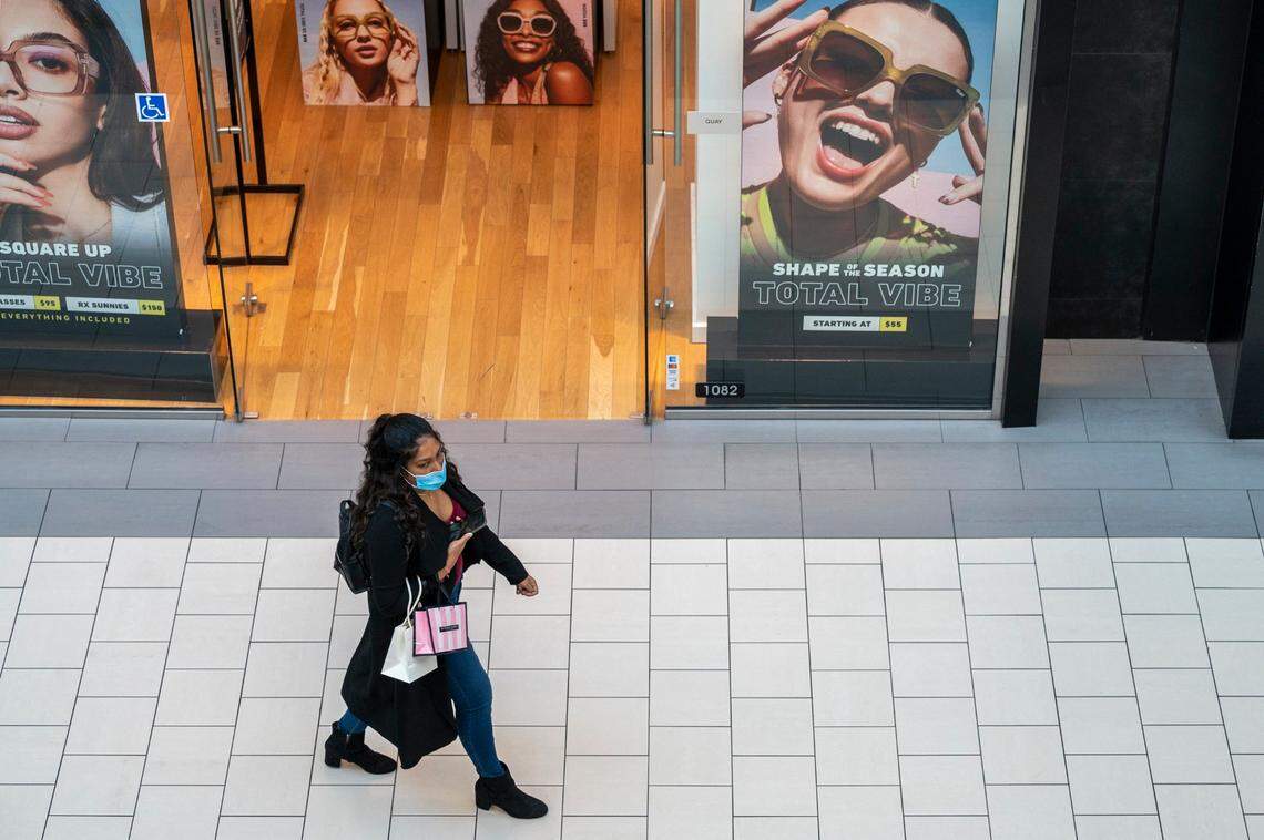 A shopper at Arden Fair mall in Sacramento wears a mask as she passes by posters with smiling models on Tuesday. California’s indoor mask mandate ends Wednesday, but teachers and students must keep masking up under state guidelines.