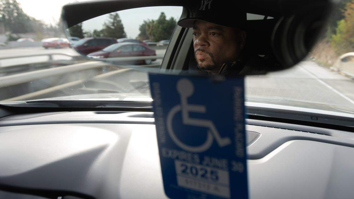 Carlos Castro’s face is reflected in the rear view mirror above his disabled placard as he drives to his San Jose gym on Dec. 15, 2023. Castro was injured in a construction accident and is been paralyzed from his chest down.