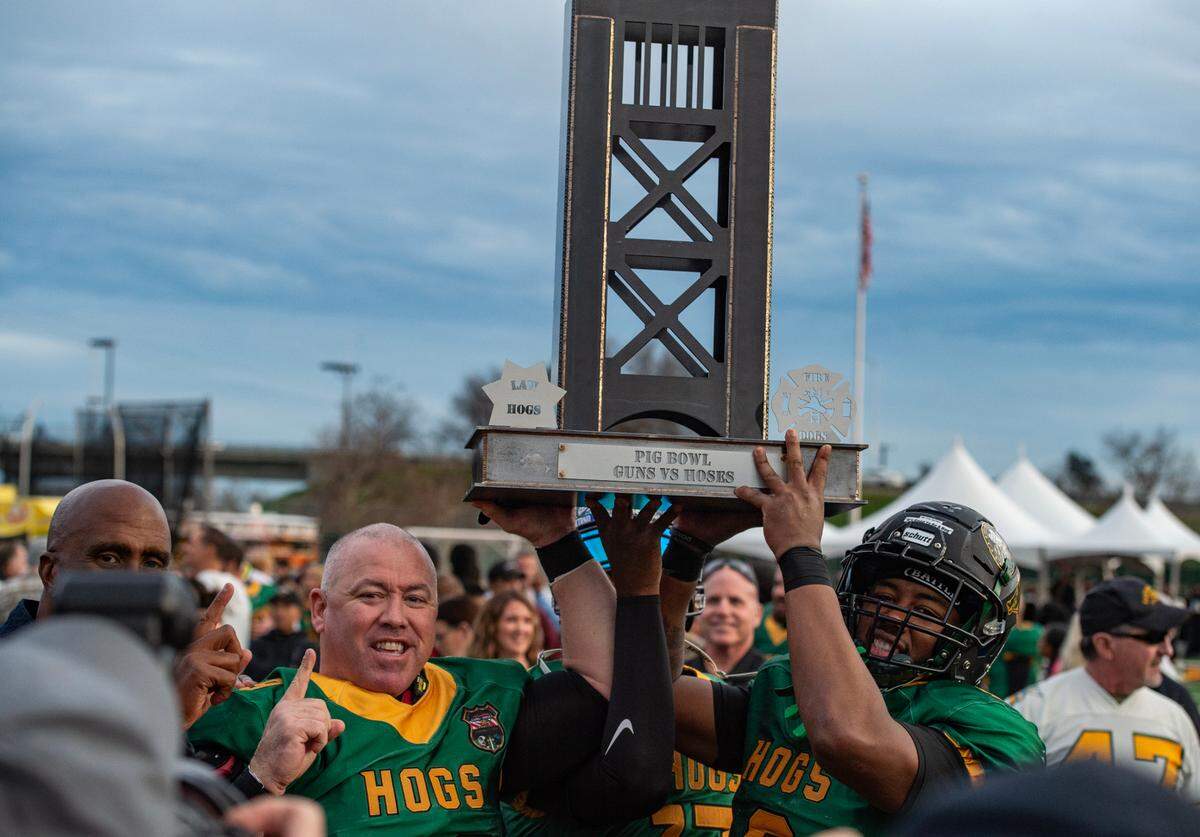Law Hogs offensive lineman Cody Cotten, left, and wide receiver Terrence McDonald hoist the Pig Bowl Guns vs. Hoses trophy after their victory in the 50th anniversary game Saturday, Jan. 27, 2024, at Hughes Stadium. 