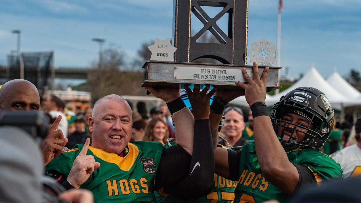 Law Hogs offensive lineman Cody Cotten, left, and wide receiver Terrence McDonald hoist the Pig Bowl Guns vs. Hoses trophy after their victory in the 50th anniversary game Saturday at Hughes Stadium.