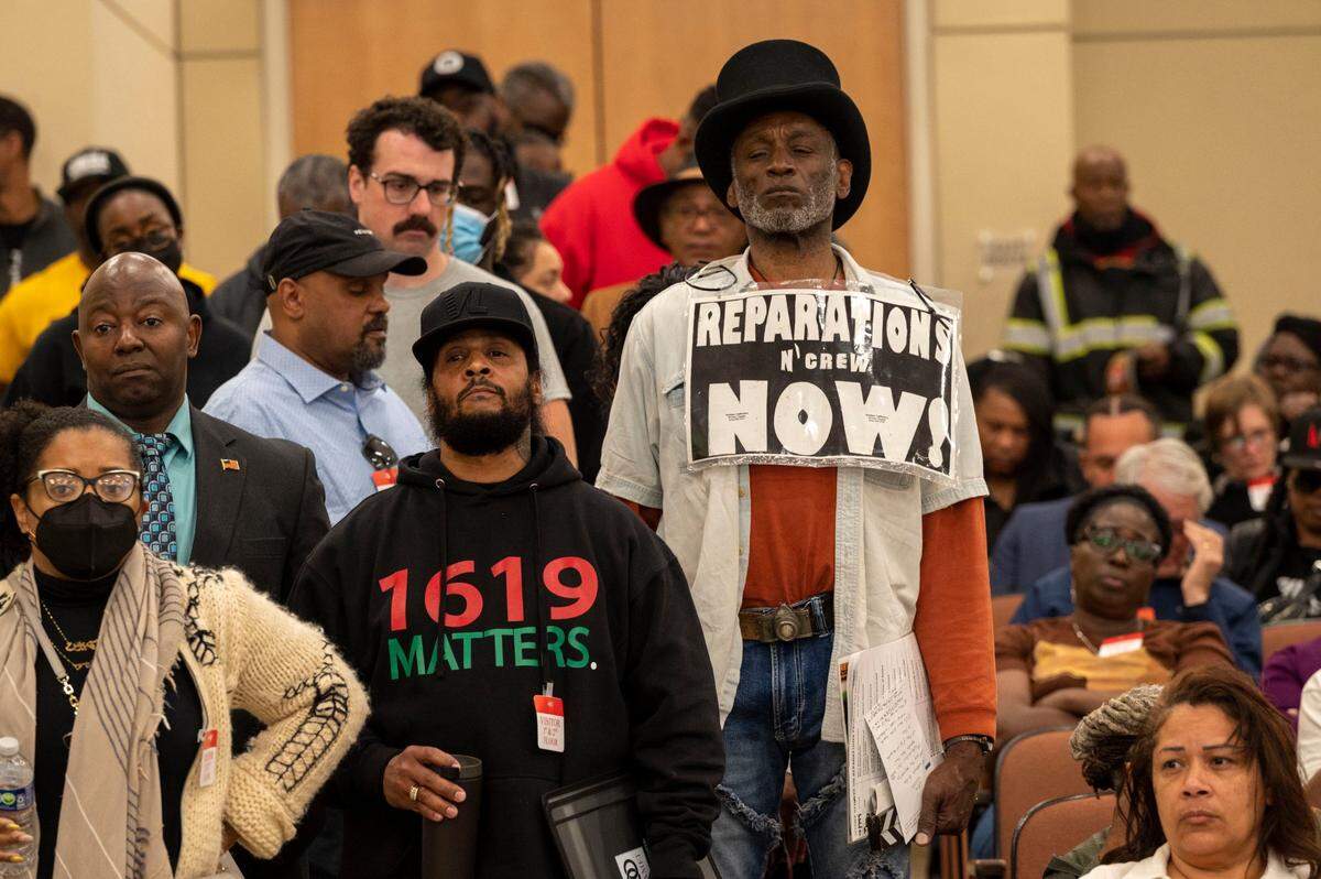 Morris Griffin, wearing a sign that says “reparations now,” waits in a line to speak during public comment on Saturday at a meeting of the California Reparations Task Force, which convened for a second day at the California Environmental Protection Agency in Sacramento to study reparations proposals for Black Californians.