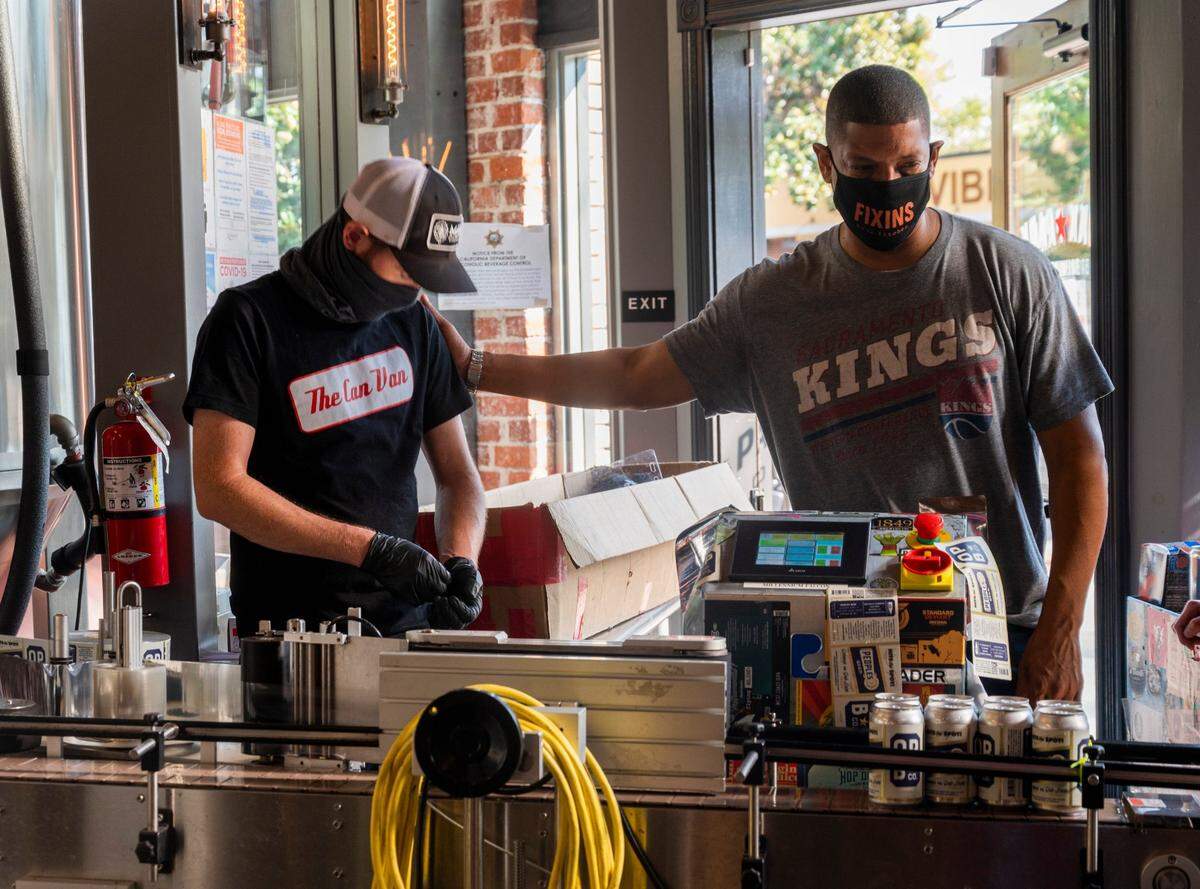 Co-owner of Oak Park Brewing and former Sacramento mayor Kevin Johnson, right, gestures to John Newman of the Can Van while canning People’s Beer on Aug. 27, 2020.