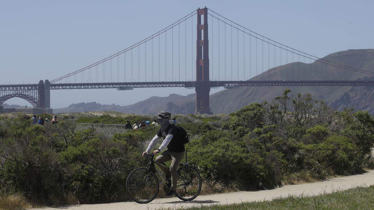 A man wears a mask while riding a bicycle in front of the Golden Gate Bridge during the coronavirus outbreak in San Francisco, Sunday, May 3, 2020. (AP Photo/Jeff Chiu)