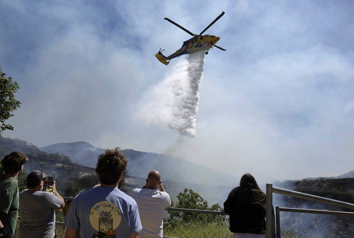 Residents look on as a Ventura County Fire Department helicopter drops water on the Sandy Fire on Monday, May 18, 2026, in Simi Valley. The fast-moving fire has prompted evacuation orders and comes as state fire officials warn that cured grasses and brush across California are ready for ignition after several wet years of growth.
