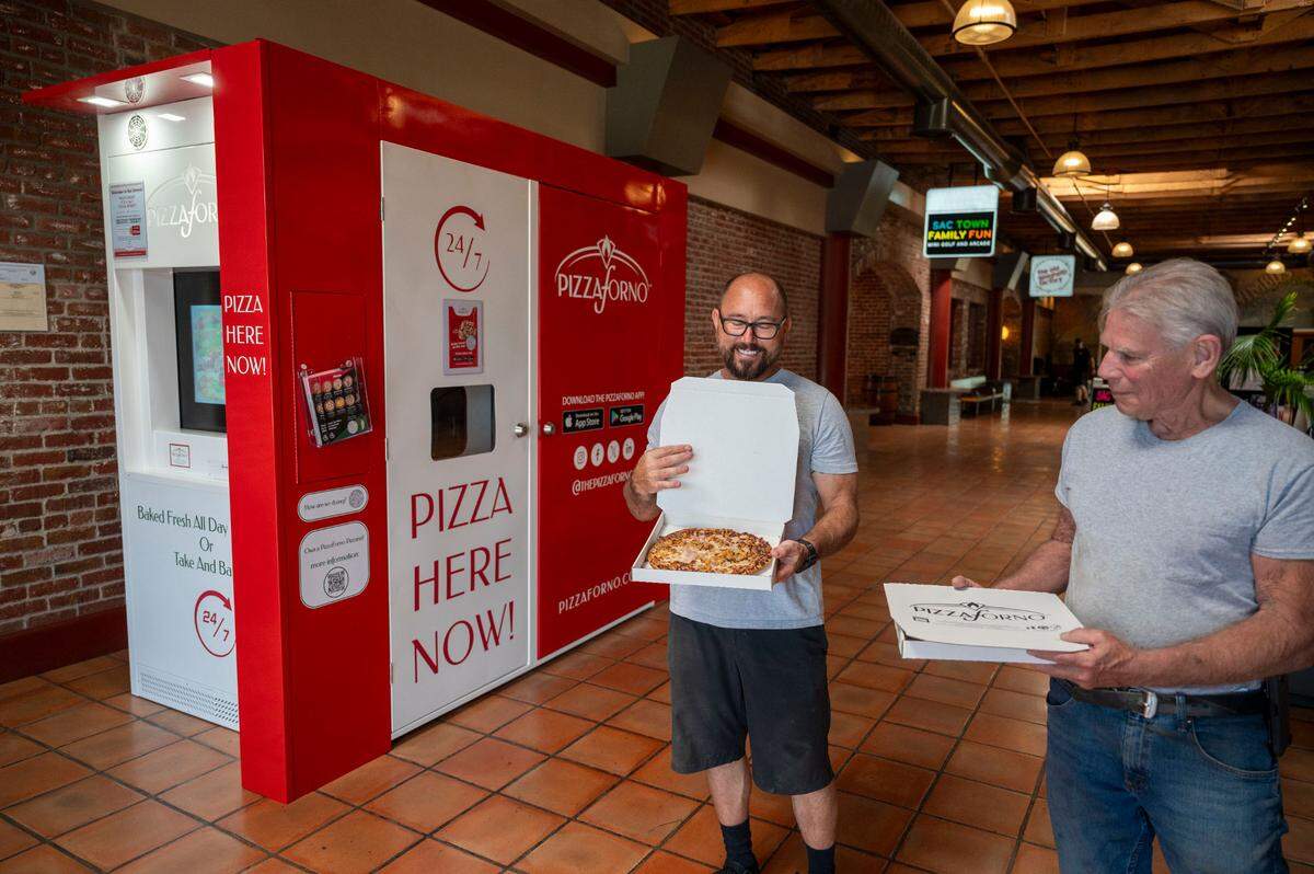 Patrick Calderone, left, and Dennis Ruggiero get lunch from PizzaForno, an automated vending machine that offers made-to-order pizza day and night, in the lobby at Nimbus Winery in Rancho Cordova on Tuesday, Aug. 20, 2024.