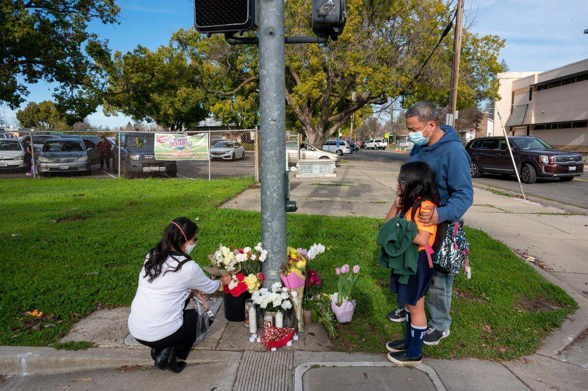 Cherie Dumag adds flowers to a makeshift memorial while her husband Ronnie stands with their daughter Aniela, 10, a fourth grader at Phoebe Hearst Elementary School on Friday, Jan. 14, 2022. A Phoebe Hearst parent pedestrian was tragically killed in a car accident during school pickup at in front of the school Thursday on the corner of Folsom Boulevard and 60th Street in East Sacramento.