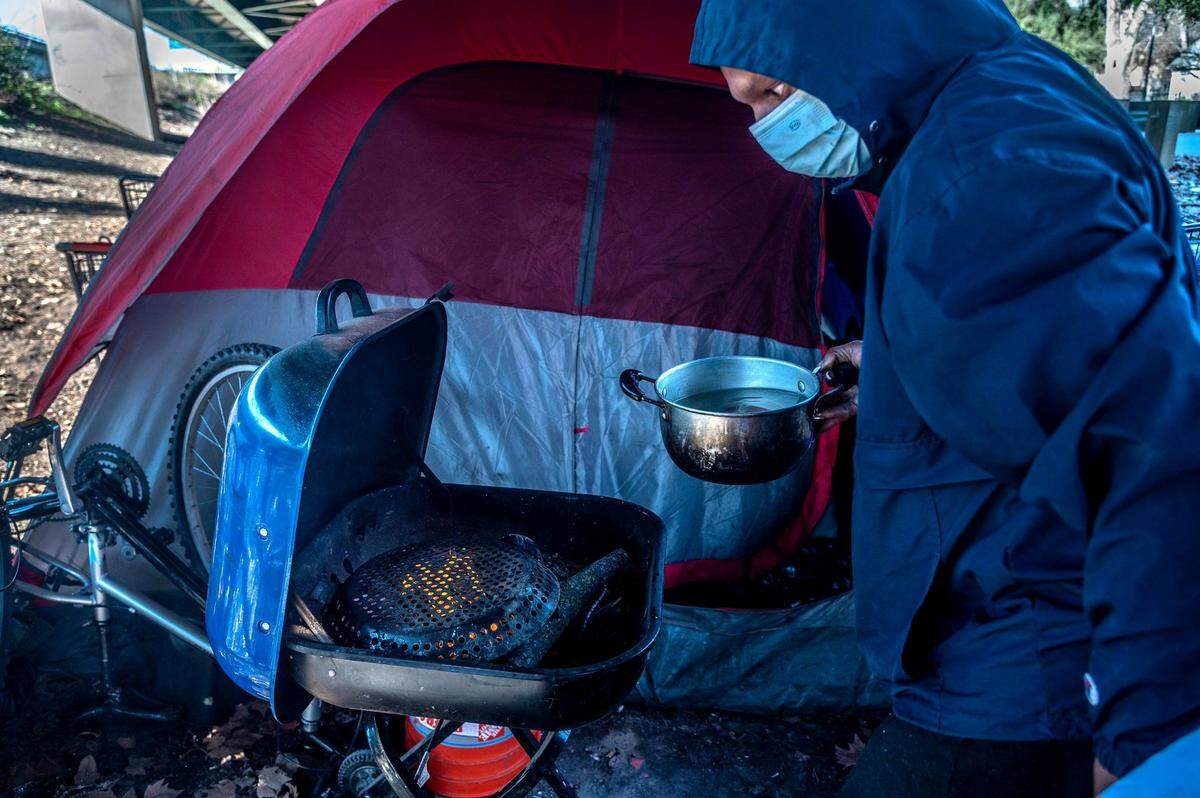 Timell Brown burns a paper plate under some tree branches to start a fire in her outdoor grill to heat water to clean dishes.