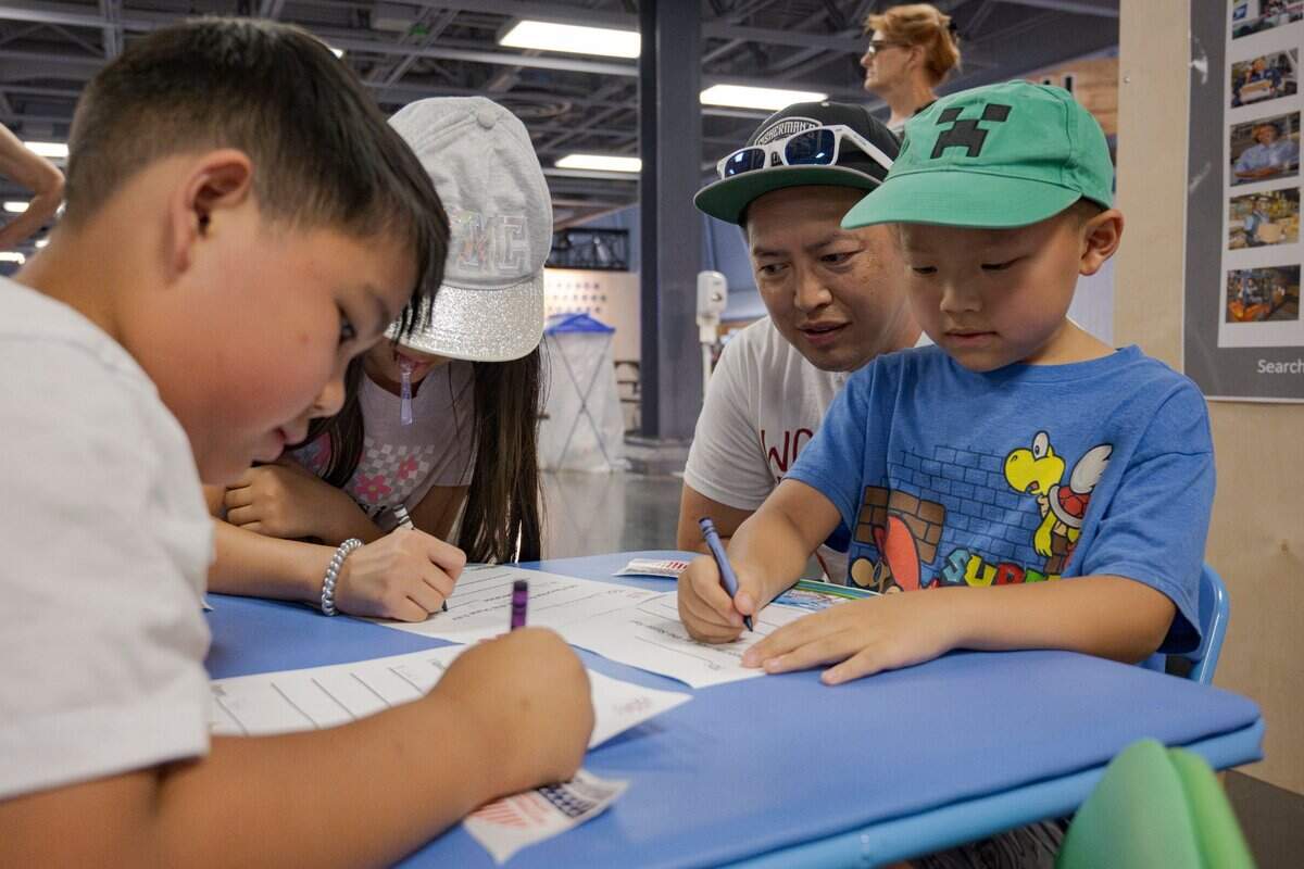 Alee Moua, center, helps his children write letters at the post office inside the California State Fair Tuesday in Sacramento.