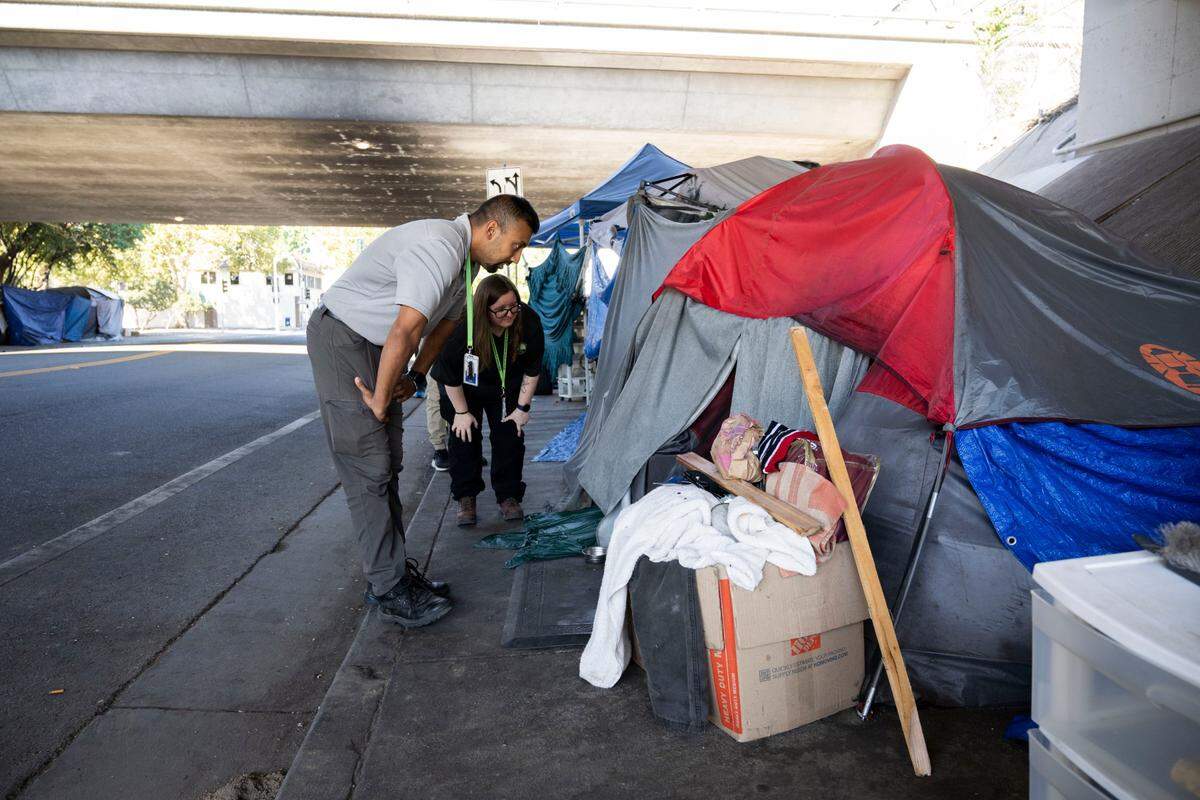 Jawid Sharifi and Hailey Weaslee, neighborhood resource coordinators for the city of Sacramento, talk to a homeless person in a tent on the E Street sidewalk on Wednesday, Oct. 5, 2022. The outreach team was informing campers about a new city ordinance that requires four feet of clearance so that wheelchair users won’t be obstructed on the sidewalk.