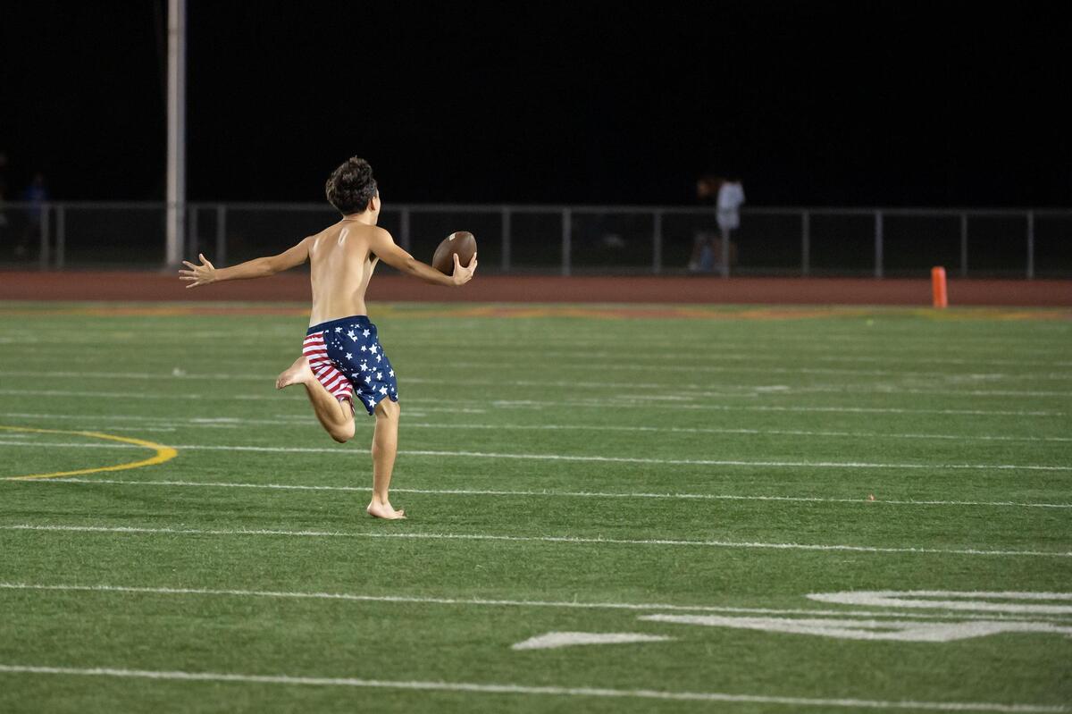 A shirtless student runs off the field with the game ball in the third quarter as Jesuit and Christian Brothers play in the Holy Bowl on Saturday, Sept. 10, 2022, at Sacramento City College.
