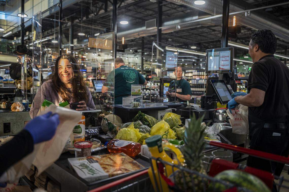 Lisa Trn smiles as employees bag her groceries as early morning light catches her face behind a plastic shield at a checkout stand to help mitigate the spread of coronavirus, Wednesday, April 15, 2020, on opening day at the new Raley’s in South Land Park.