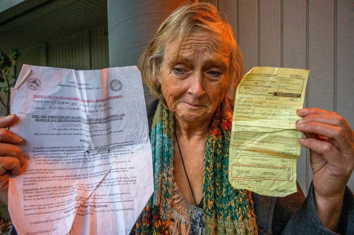 Carol Dutcher, 60, holds a citation for littering and a notice to vacate an encampment issued in November by Sacramento County park rangers as she takes shelter from the rain in Sacramento. Dutcher said she was on a list for housing, but she was worried her citations could turn into warrants that would disqualify her. “It wasn’t litter, it was my stuff – my possessions, my sleeping bag,” she said.