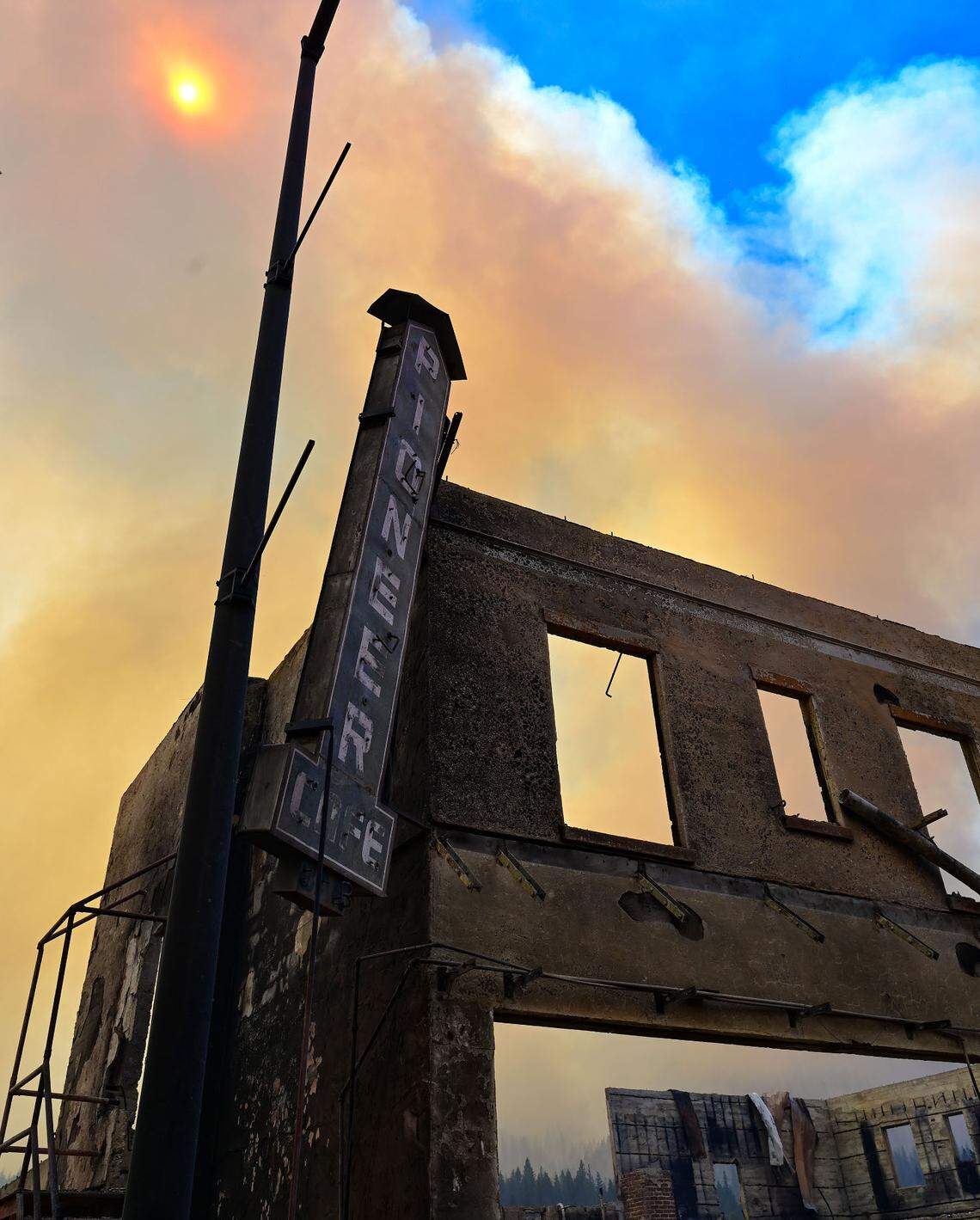 The sign for Pioneer Cafe hangs on the facade of the Sierra Lodge on Main Street in Greenville on Aug. 5 after the Dixie Fire, still burning in the background, leveled the town. The facade collapsed minutes later.
