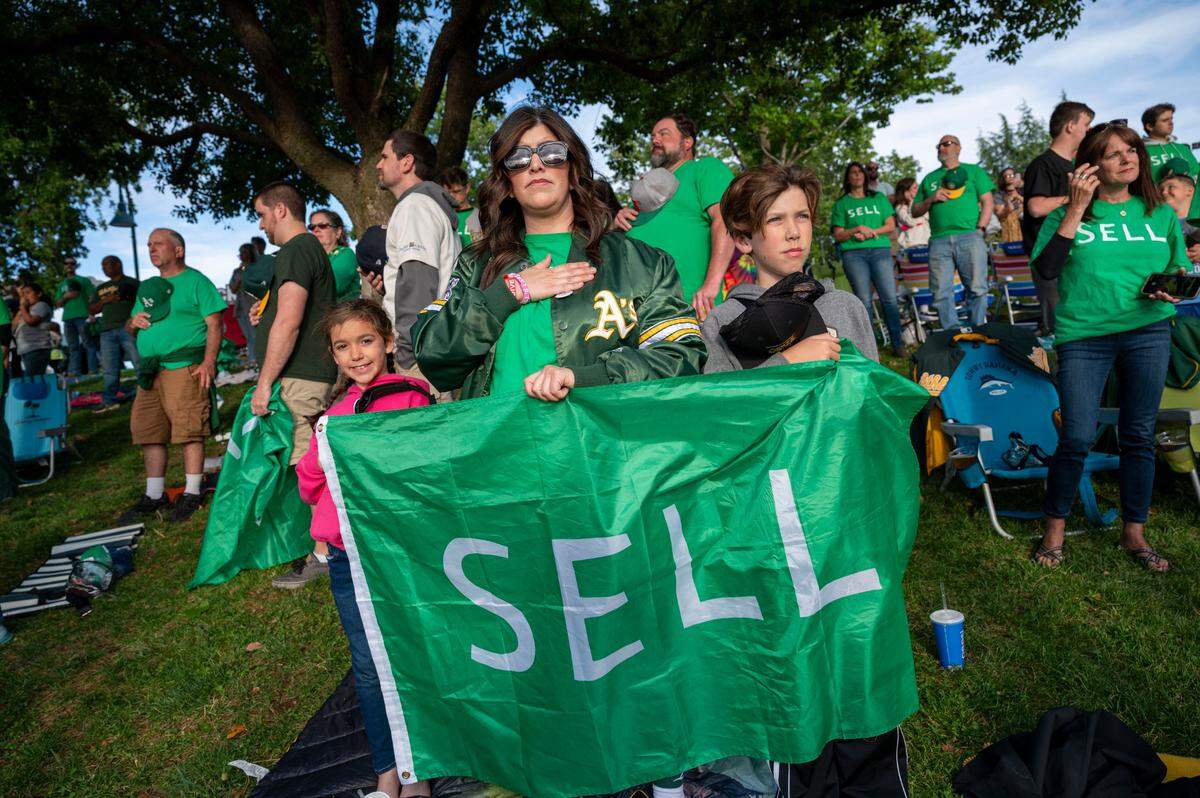 A’s fan Kristen Cutberth of Roseville holds a “SELL” flag with her children Lucy, 7, left, and Logan, 10, during a protest Saturday at the River Cats-Aviators game.