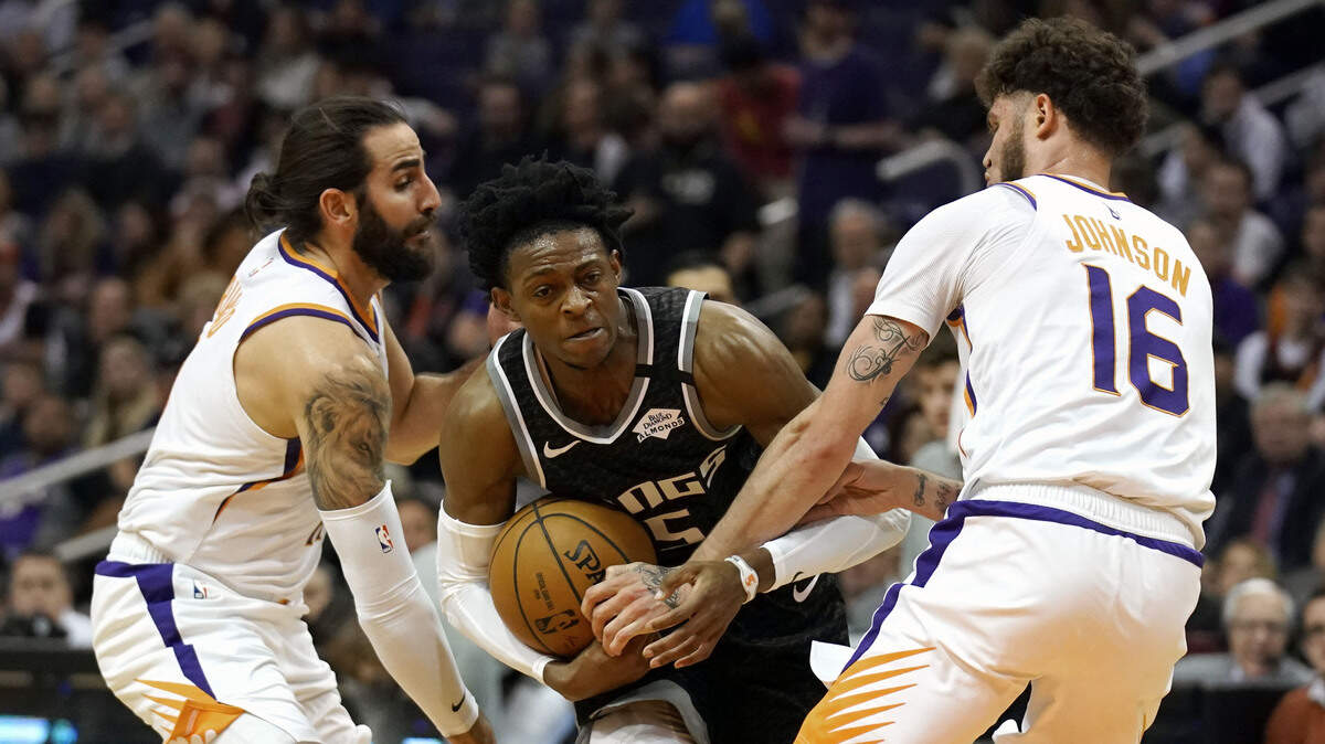 Sacramento Kings guard De’Aaron Fox (5) drives between Phoenix Suns guard Ricky Rubio and Tyler Johnson (16) in the first half during an NBA basketball game, Tuesday, Jan. 7, 2020, in Phoenix. (AP Photo/Rick Scuteri)