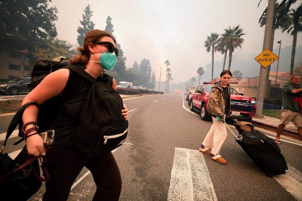 People evacuate at Sunset Boulevard and Palisades Drive in Pacific Palisades after a brush fire quickly consumed vegetation on Tuesday, Jan. 7, 2025, with flames fueled by gusting Santa Ana winds.