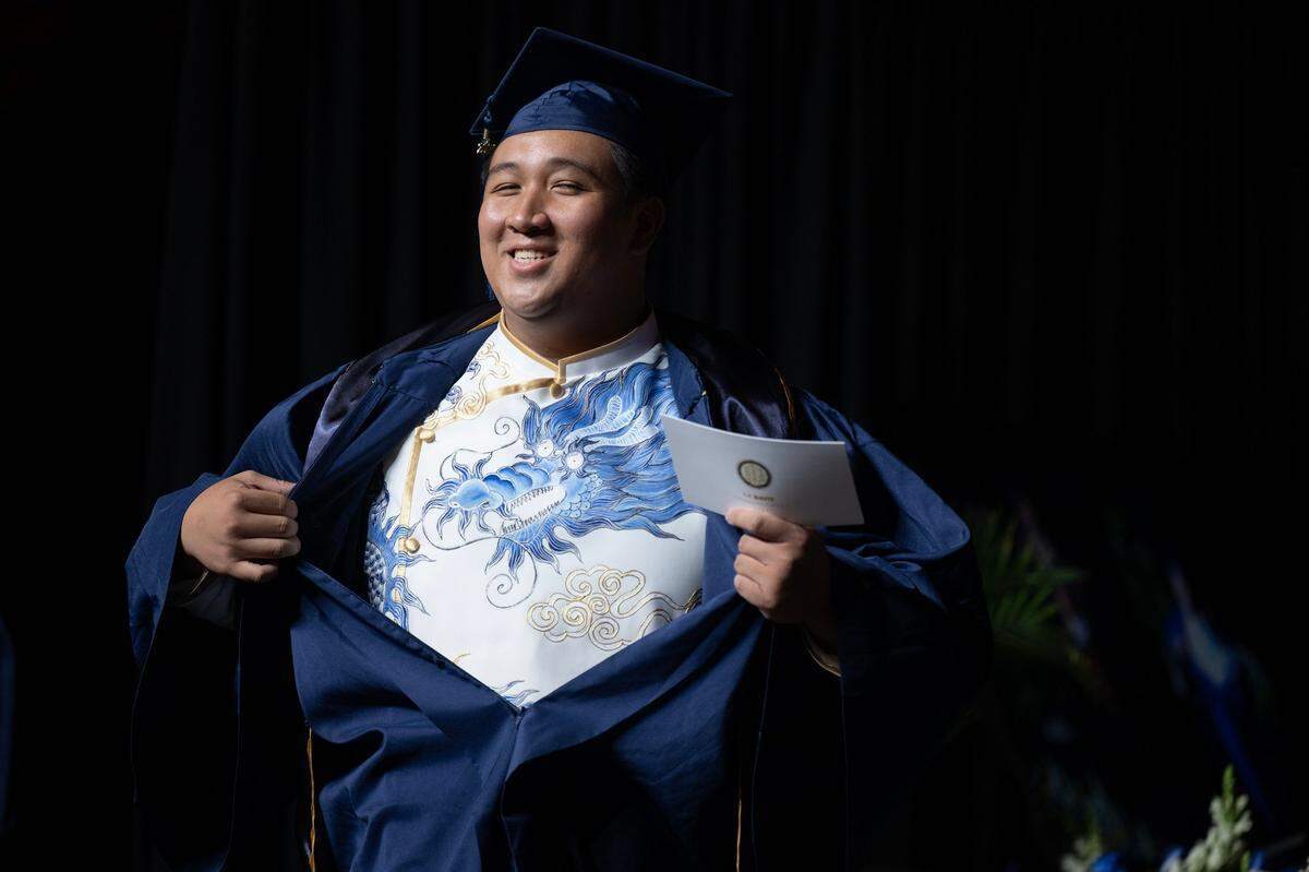 Jimmy Tran, graduating with a degree in mechanical engineering, shows off a blue dragon on his shirt after his name is announced while he walks on stage to receive his diploma during the 2024 UC Davis commencement ceremony at Golden 1 Center on Friday.