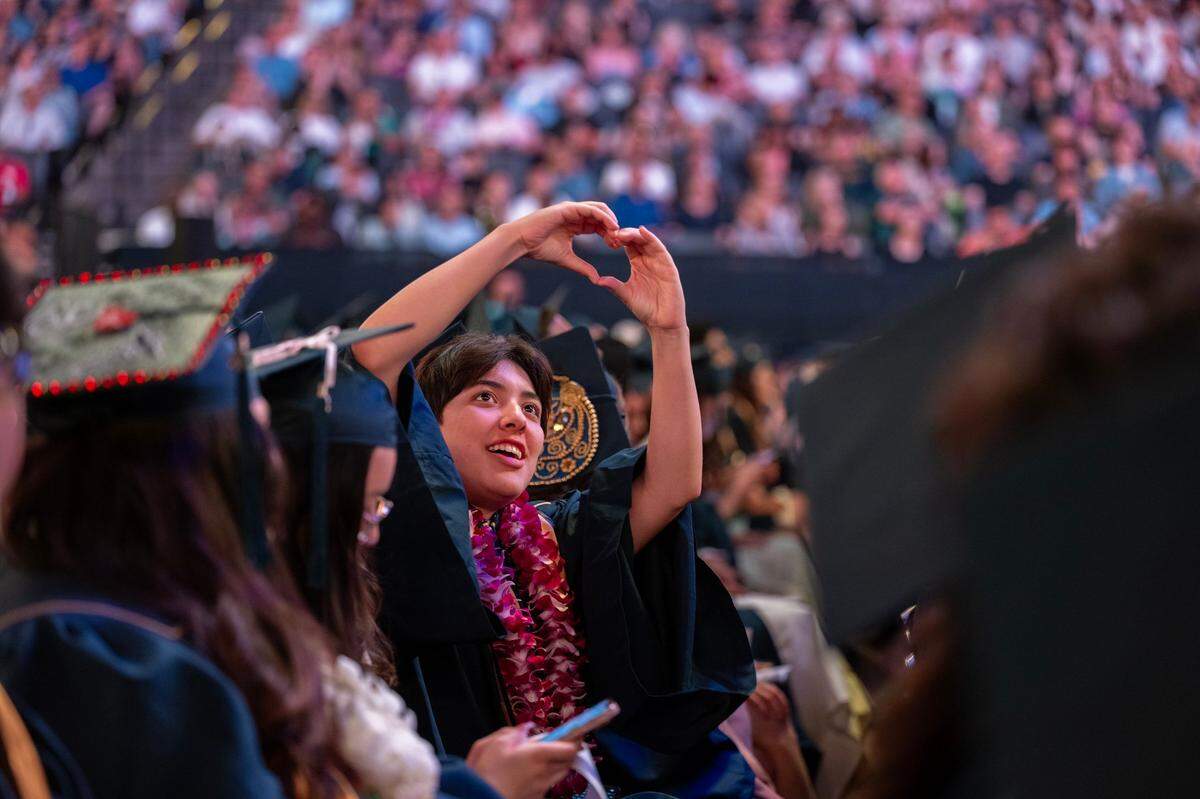 Malinalli Elizabeth Ortega makes the universal sign of love toward her family in the stands in the Golden 1 Center as the 2024 graduating class of UC Davis received their diplomas on Friday.