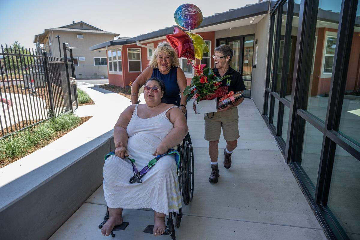 Deborah Casillas pushes her daughter, Holly Porter, in her chair, alongside Tracey Knickerbocker with Hope Cooperatives. Porter, a quadriplegic who was living in a hospital bed at Camp Resolution, got the keys to her new apartment Thursday, after actively seeking housing for a year and a half.