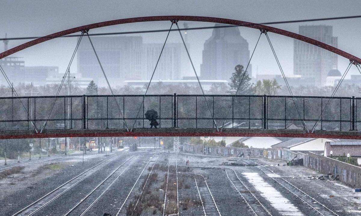 A person walks with an umbrella on the pedestrian and bicycle bridge that connects Sacramento City College and Crocker Village as rain falls in Sacramento on Tuesday, March 28, 2023.