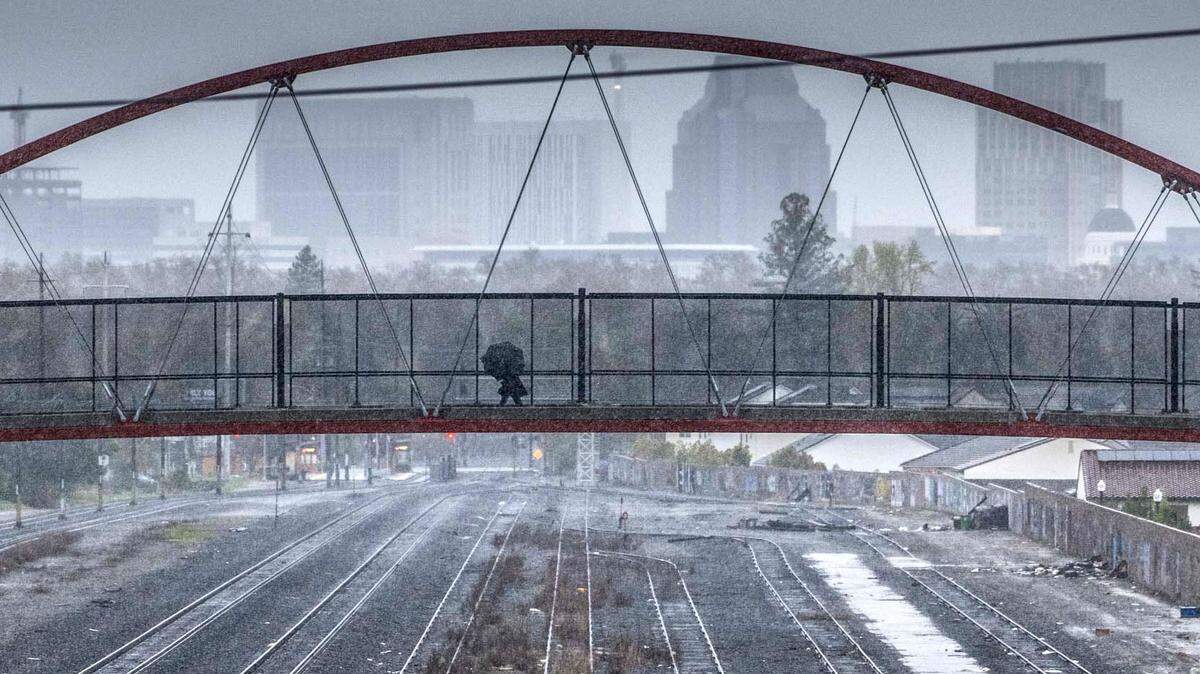 A person walks with an umbrella on the pedestrian and bicycle bridge that connects Sacramento City College and Crocker Village as rain falls in Sacramento on Tuesday, March 28, 2023. A little more than an inch of rain is expected during this week’s storm, said National Weather Service meteorologist Scott Rowe.