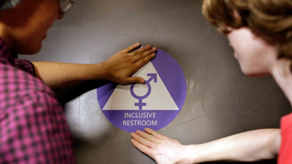 In this May 2016 file photo, two Seattle students place a new sticker on the door at the ceremonial opening of a gender neutral bathroom at Nathan Hale High School. (AP Photo/Elaine Thompson)