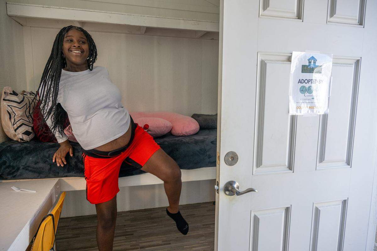 Toriana Thompson, 23, hops up onto the bed of her tiny cabin at The Grove homeless shelter for young people age 18-24 in North Sacramento on Wednesday. Her space in the tiny-cabin community is sponsored by Life Practice Counseling Group. The $1,000 sponsorships help provide essential repairs, ongoing maintenance and the creation of a welcoming porch.