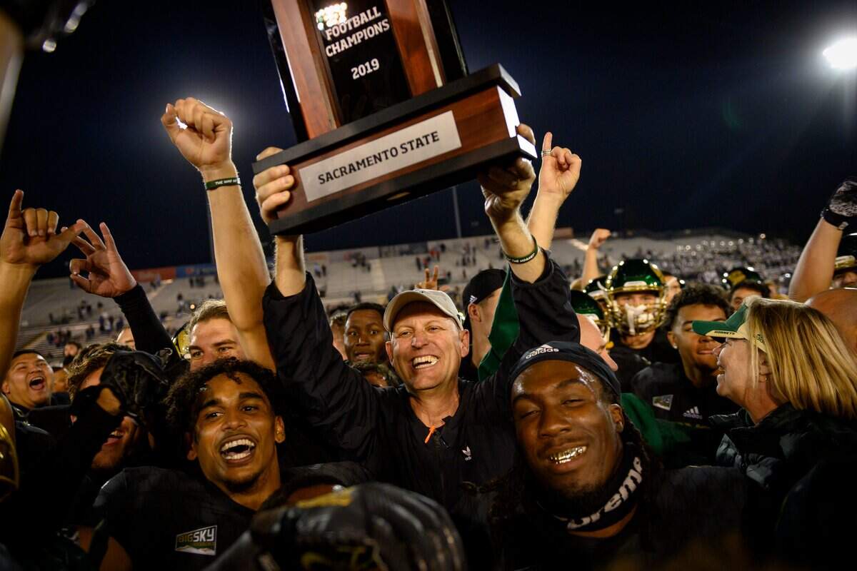 Then-Sacramento State head coach Troy Taylor celebrates by holding up the Big Sky Conference trophy while surrounded by the Hornets after their win in 2019 during the 66th Causeway Classic against UC Davis at Hornet Stadium.