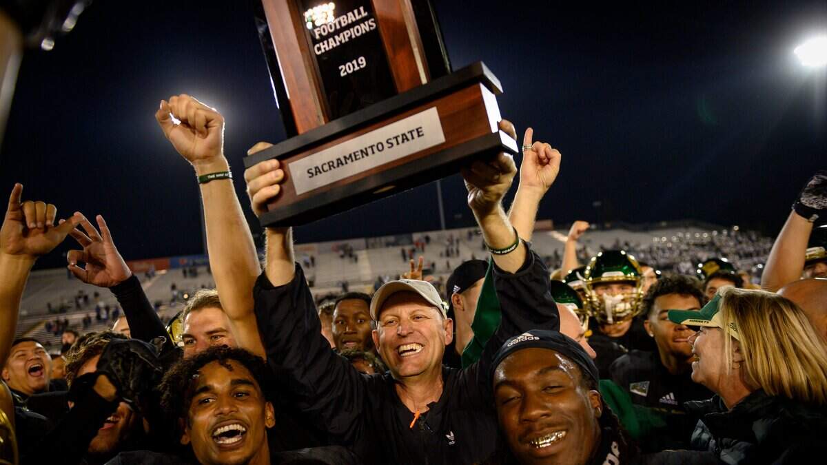 Sac State head coach Troy Taylor celebrates by holding up the Big Sky Conference trophy while surrounded by the Hornets after their win Saturday, Nov. 23, 2019, during the 66th Causeway Classic against UC Davis at Hornet Stadium.