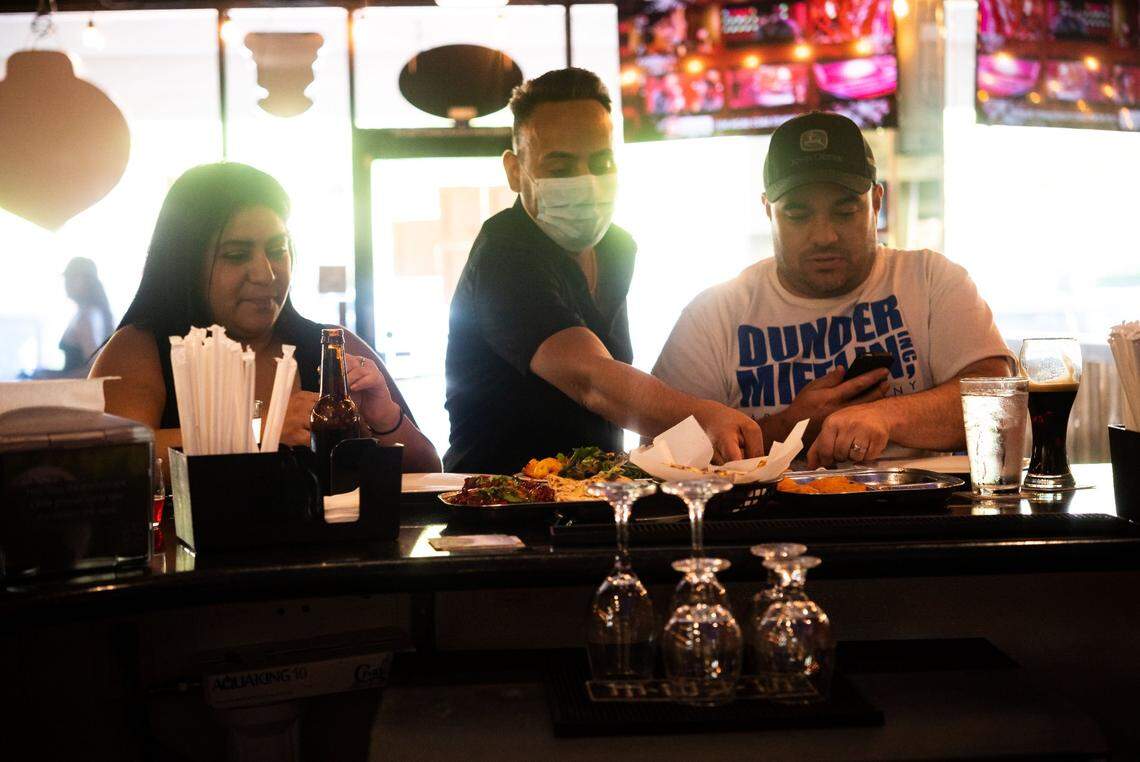 Jasdeep Singh Purewal, whose family owns and operates Hop Junction, talks with regular customers Felicia Picazo, left, and her husband Rich Knight in the Pocket neighborhood restaurant on June 27 before dine-in was again suspended because of the coronavirus pandemic. “The food is, like, amazing,” Picazo said. “I didn’t even know I liked Indian food,” she added, saying they started frequenting the bar when it served mostly burgers and pub food, but the move to Indian food after about a year made it their favorite date-night spot.