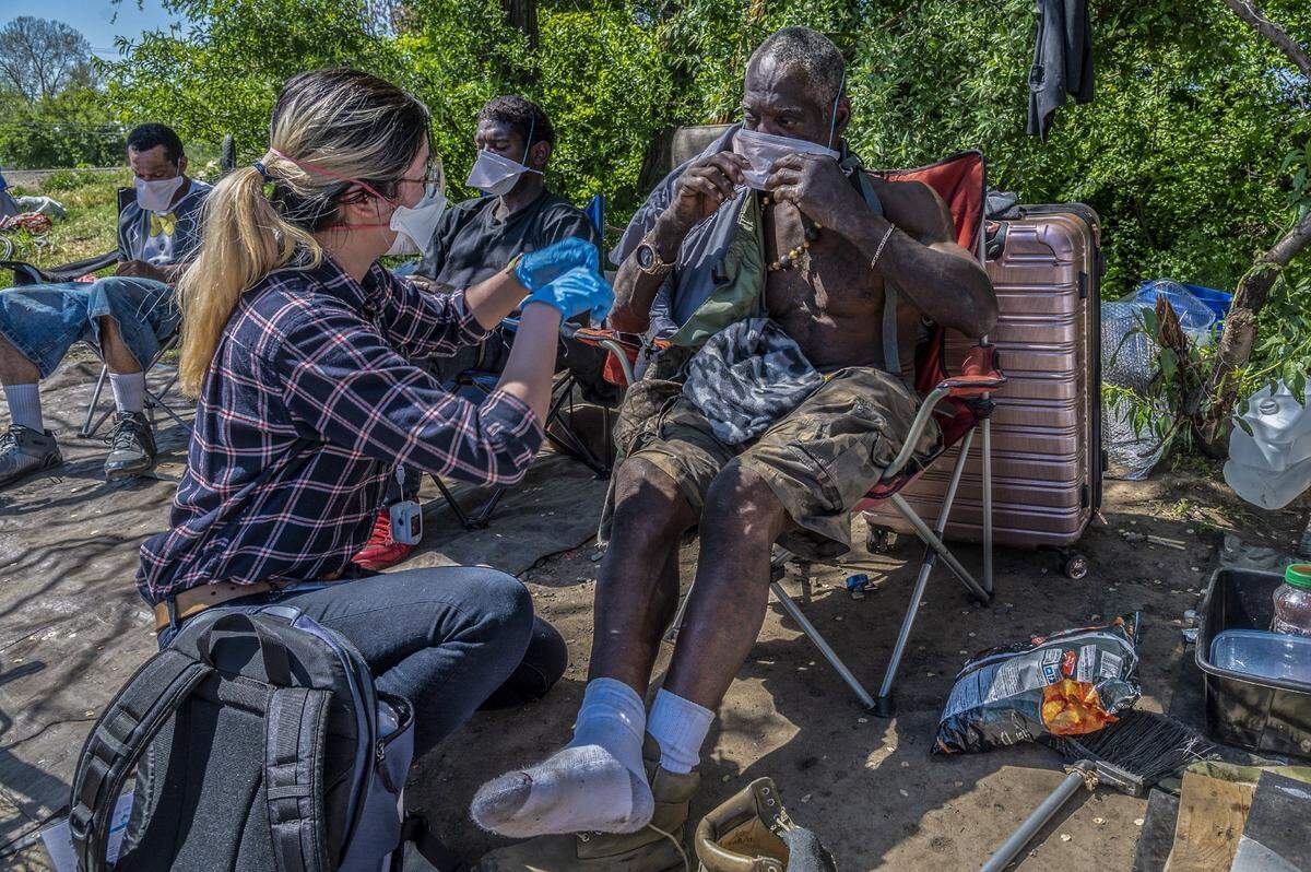 After passing out masks to the homeless med student Kim Lau, left, of Cal Northstate, educates R. Brannon, right, as she and medical students from UC Davis help provide medical help during coronavirus at an American River encampment in Sacramento on Monday, April 13, 2020.