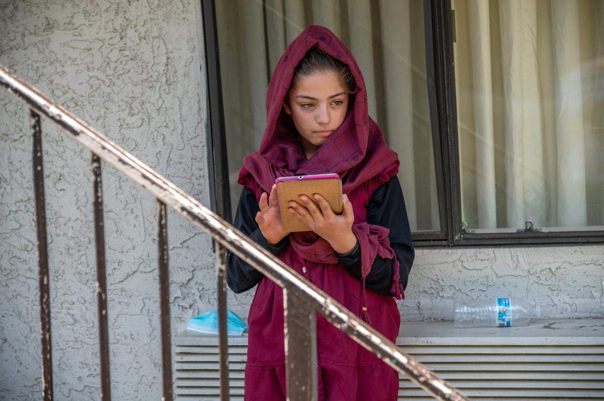 Behind a worn banister at America’s Best Value Inn in North Highlands, Zulaikha, 13, plays on a tablet, a few days after arriving in the United States. Her father Abdul said the family will enroll their children in school once they are vaccinated.