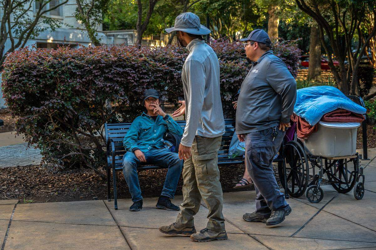 Glen Tibay, 38, who is partially deaf and homeless, sits on a bench as staff from the Sacramento City Department of Community Response approach him on Wednesday, the night before an ordinance banning sleeping outside City Hall took effect. Tibay said he couldn’t hear them well due to his disability. He said he wants to be admitted into a shelter with wraparound services to help him find a job and become self-sustaining.