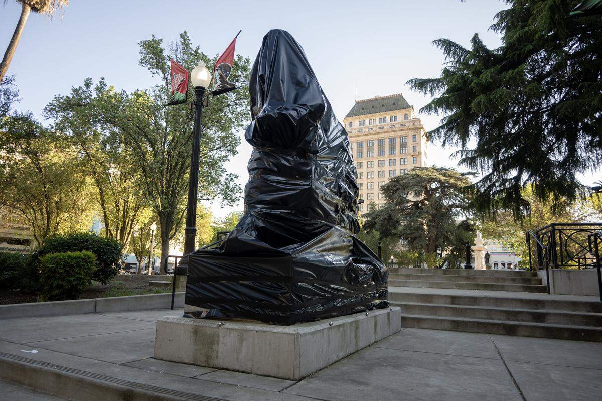 Black plastic covers the statue depicting Cesar Chavez in Cesar E. Chavez Plaza in Sacramento on Friday, March 20, 2026. City officials announced plans to rename the park after accusations of rape and sexual assault by the civil rights leader surfaced. The Legislature is renaming Cesar Chavez Day to Farmworkers Day. 
