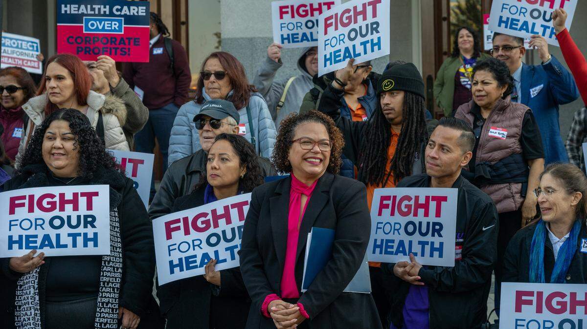 Assemblymember Mia Bonta, chair of the Assembly Health Committee, center, smiles after speaking at a “Fight for Our Health” rally at the state Capitol on Wednesday, Jan. 14, 2026, in Sacramento. A tax proposal Bonta carried to make corporations whose employees rely on the state for healthcare chip into a Medi-Cal fund hit a legislative speed bump Thursday. May 14, 2026, when the Appropriations committee put the bill on hold. 