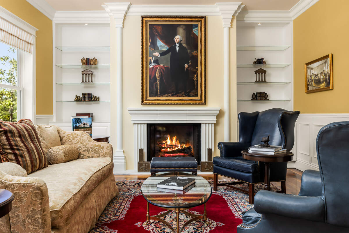The formal living room, anchored by a fireplace and views toward the pond, is part of a layout designed for large-scale entertaining.