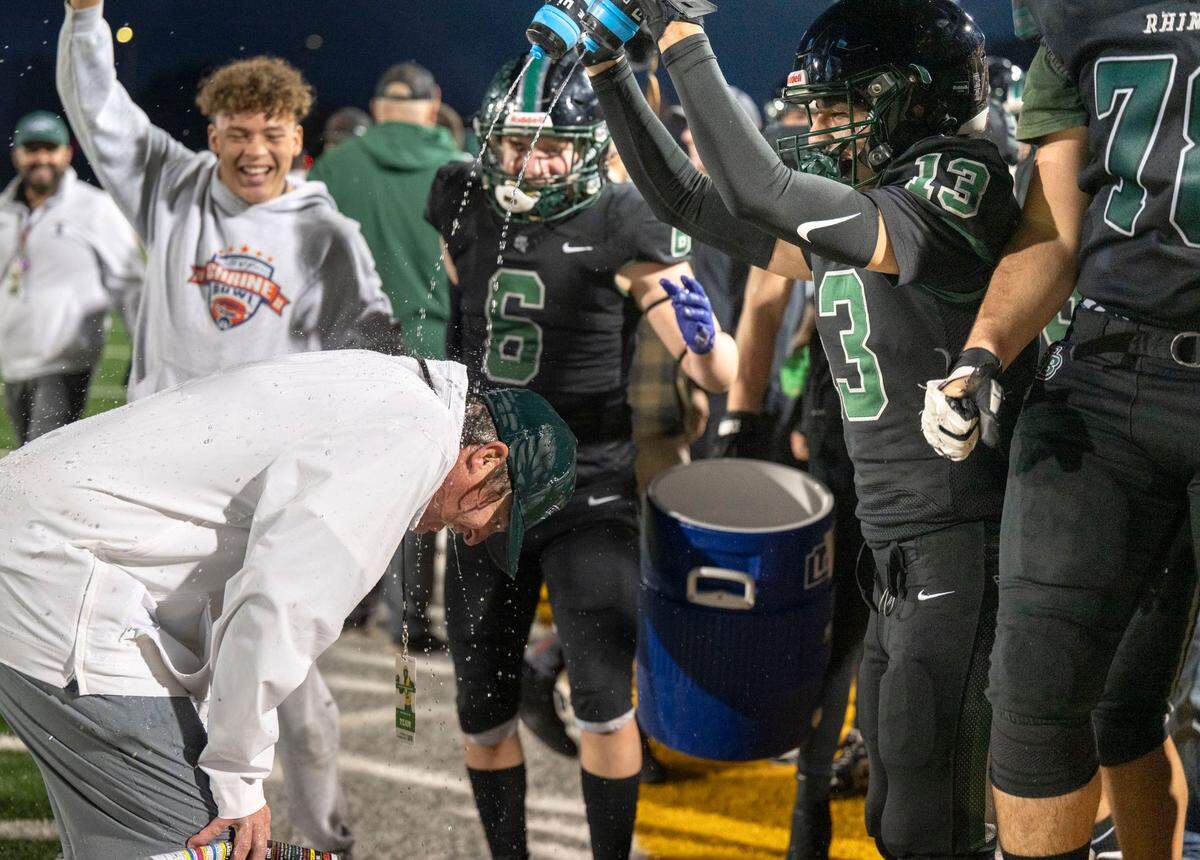 The Twelve Bridges Raging Rhinos’ Joseph Alkhudr (13) pours a little extra water on coach Chris Bean as he recovers from an ice water bucket dump on the sidelines as the clock winds down on team’s victory in the Sac-Joaquin Section Division IV championship game on Nov. 29, 2024, at Hughes Stadium in Sacramento.