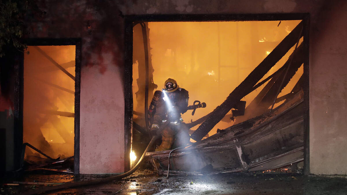 A firefighter works the scene of a wildfire-ravaged home Thursday in Santa Clarita. Fast-growing fires across California have forced thousands of people to evacuate as dry winds and high heat feed the flames.