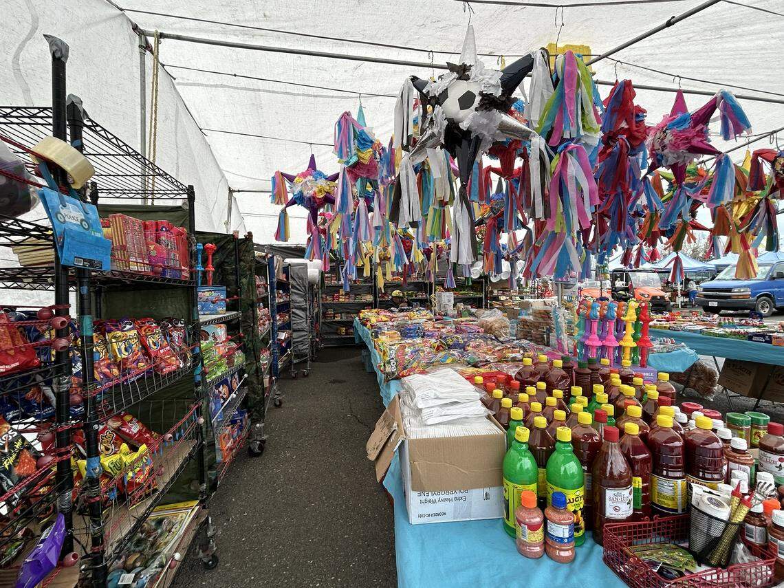 A Galt Flea Market vendor hangs colorful pinatas from the ceiling of their tent with rows of snacks.