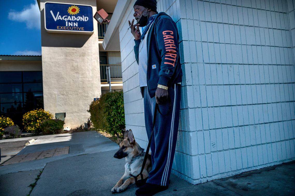 Bennie Rogers, 68, takes a smoke break with his friend’s dog King outside the Vagabond Inn where he found temporary housing through Project Roomkey on Thursday, March 25. He’s not permitted to smoke in his room and can only remove his mask to smoke if he’s 12 feet away from others.