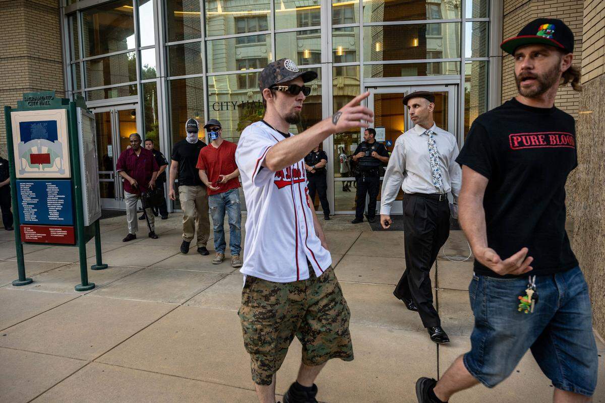 Jeffrey Erik Perrine, far right wearing a “pure blood” T-shirt, and Ryan Messano, second from right in tie, leave Sacramento City Hall on Tuesday after a group stormed the City Council meeting demanding Messano leave. After two adjournments, the chamber was cleared and public comment done by phone.