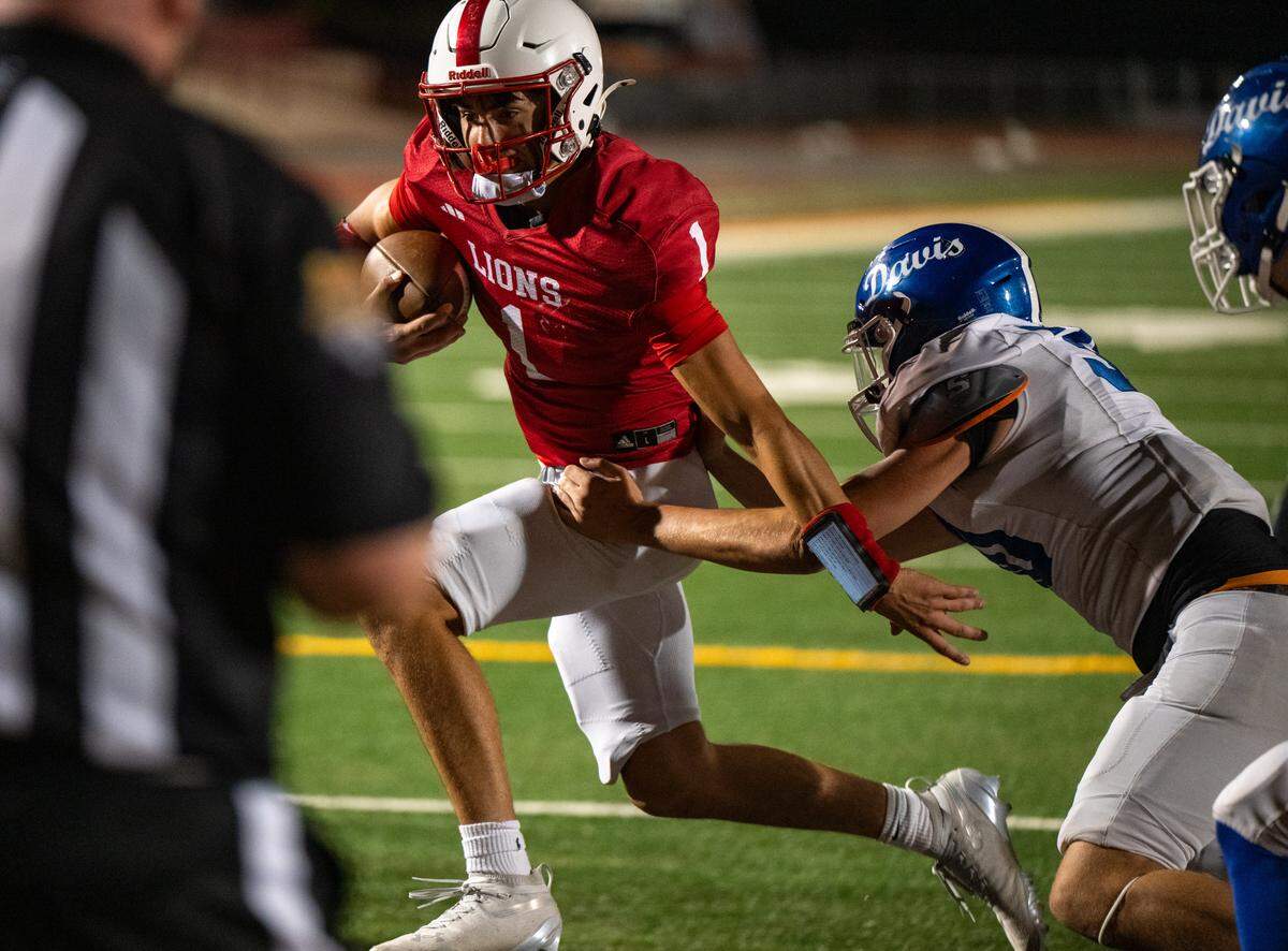 McClatchy Lions quarterback Josiah Hutchison (1) escapes the clutches of the Davis Blue Devils’ Carter Post (30) on his way to a touchdown in the second half on Friday at Hughes Stadium in Sacramento. 